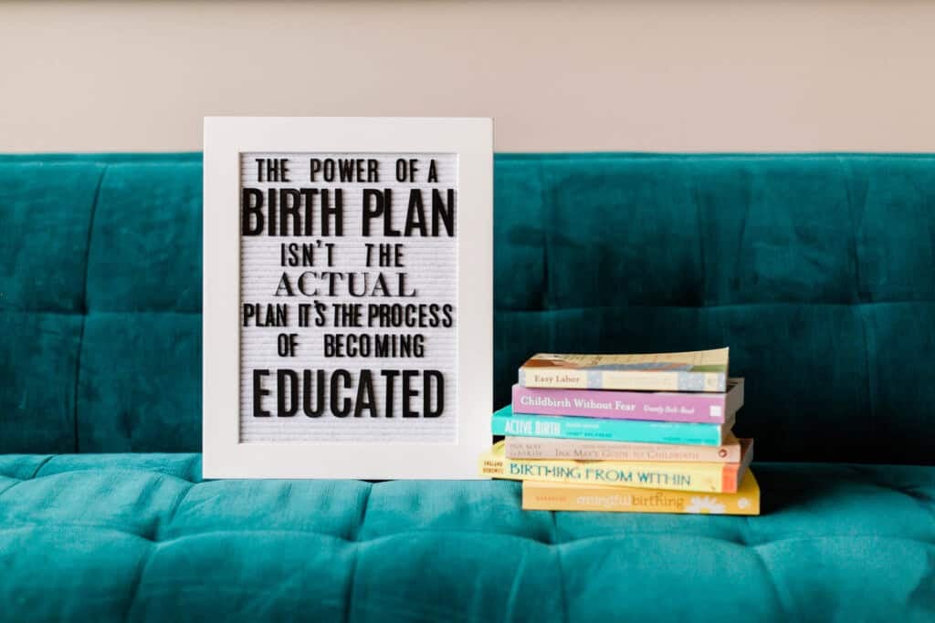 A framed sign with the quote The power of a birth plan isnt the actual plan. Its the process of becoming educated sits on a teal couch next to a stack of pregnancy and childbirth books—perfect inspiration to create your birth plan.