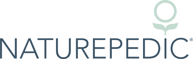 Image of the Naturepedic logo. The text "NATUREPEDIC" is written in bold, uppercase, dark blue letters. Above the text is a symbol consisting of a circle with two leaves underneath, also in dark blue, reflecting its commitment to an eco-friendly nursery.